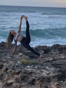 A woman is doing yoga on the rocks by the ocean.