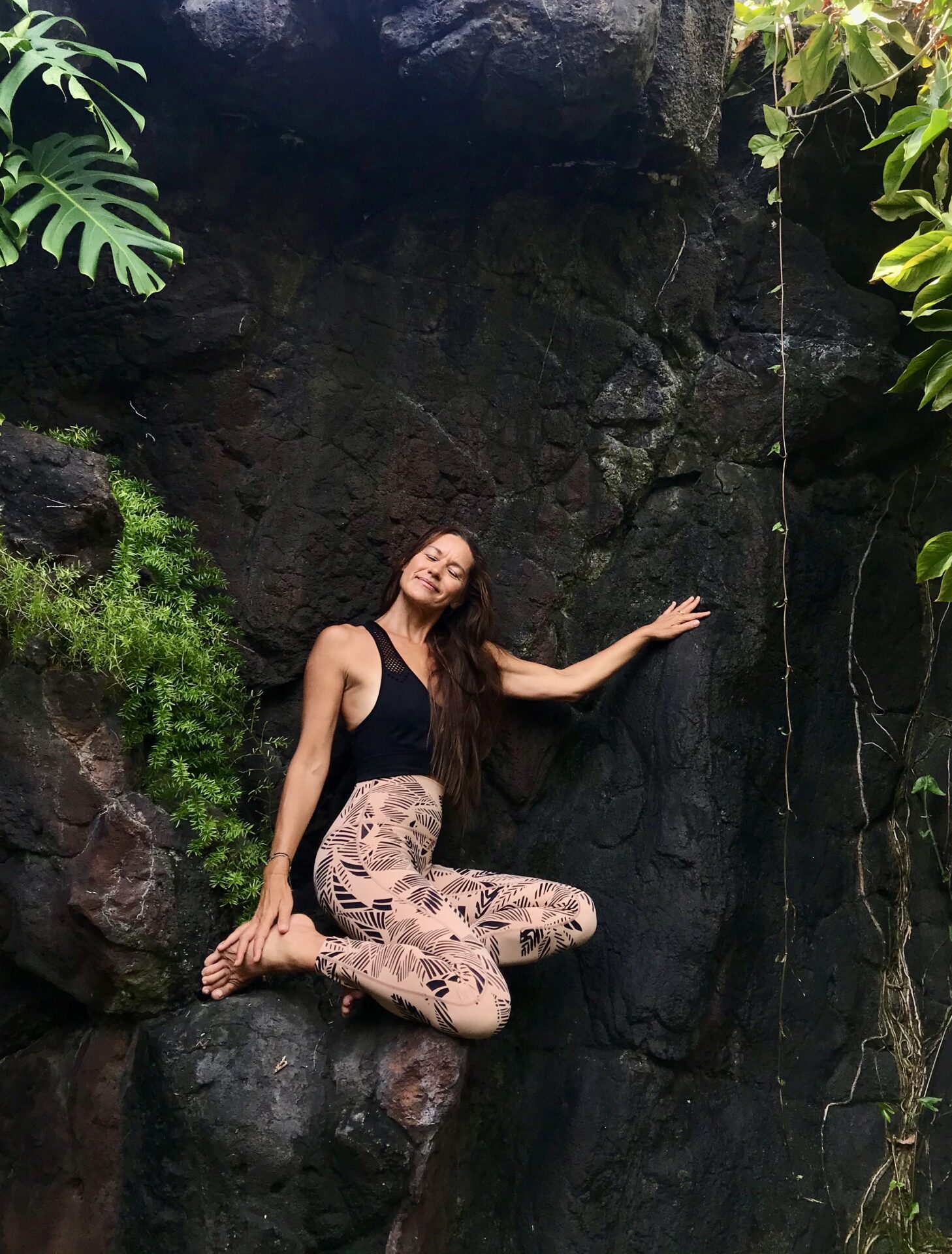 A woman sitting on the ground in front of a rock wall.