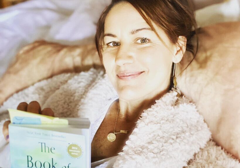 A woman laying in bed holding an open book.